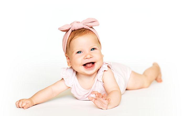 A picture of a smiling baby laying on its stomach, looking at us